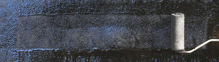 Roofer paints the surface of asphalt bitumen with a roller brush