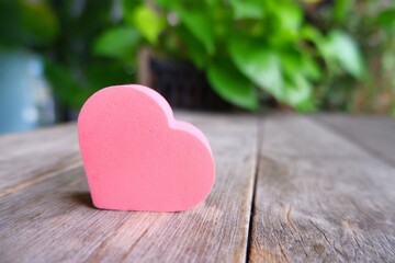 Pink heart-shaped sponge on wooden table on natural light blur background.