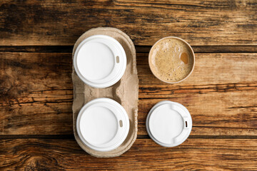 Fototapeta na wymiar Takeaway paper coffee cups and cardboard holder on wooden table, flat lay