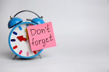 Alarm clock and reminder note with text Don't forget on light grey background. Space for design