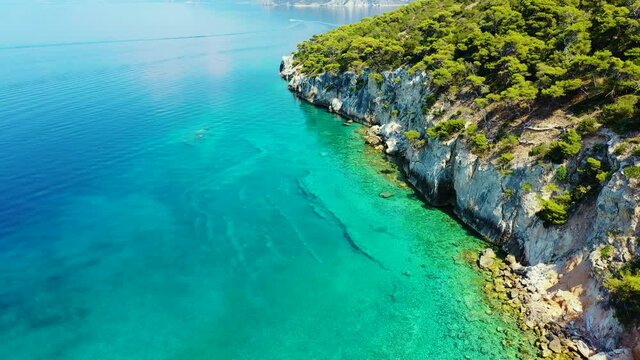 Drone flying backwards over the sea, near a beach in Mikra Strava in Greece. There is a speedboat sailing fast over the sea, in the background. It is a beautiful sunny summer day.