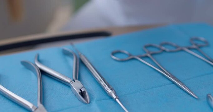 Dental scissors, dental probes, scaler, mirror, braces archwire, tweezers are laying on the table and a medical worker is taking out the dental mirror and scaler from the table.