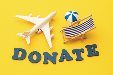 Word from wooden letters, toy plane, beach umbrella and deck chair on yellow background, vacation donation concept