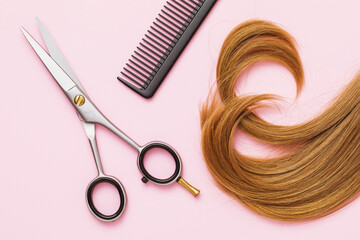 Barber scissors, comb and a lock of curly blond baby hair on a pink background