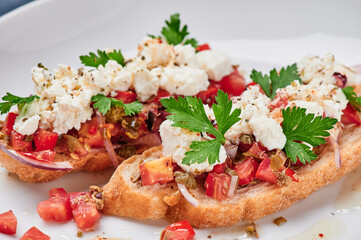 Beautiful bruschetta with feta cheese and tomatoes on a white plate close up. Space for text. High quality photo