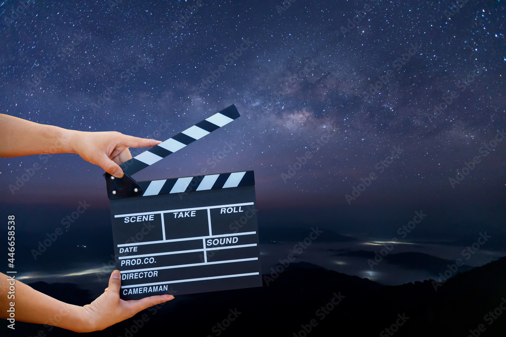 Wall mural man hands holding movie clapper on milky way , stars and mountains. shown slate board. use the color