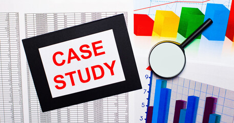On the table there are reports of multi-colored charts, a magnifying glass and a sheet of paper in a black frame with the text CASE STUDY. Business concept