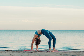 a young attractive Asian woman practicing yoga performs a stretching exercise on the beach