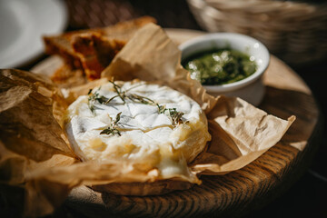 Oven baked camembert cheese with rosemary and pesto sauce on baking paper. Homemade grilled brie...