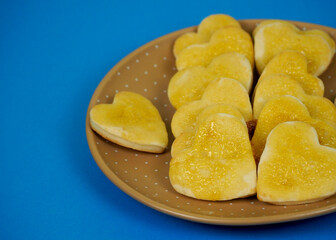 a few pieces of heart-shaped cottage cheese cookies, spread with yellow jam on top, lie in a brown plate with polka dots on a blue background. side view . gluten-free homemade cakes