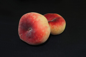 two pink fig peaches lie on a black background