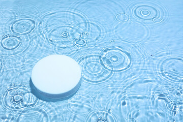 Empty white circle podium on transparent clear calm blue water texture with splashes and waves in...