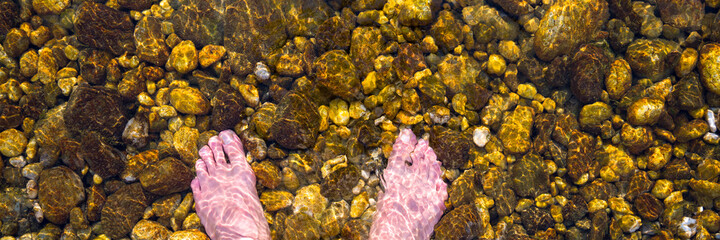 bare feet immersed in water, on river pebbles. Concept. peace, tranquility, well-being, relaxation, freshness, enjoyment, relax. Banner