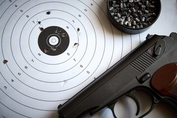 A sports pistol on the background of a target with bullet holes and lead bullets.