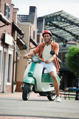 young african american man smiling at camera while sitting on scooter