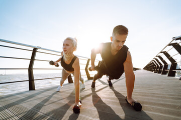 Healthy lifestyle. Young beautiful couple doing sports exercises at the beach pier. Sport, Active life.