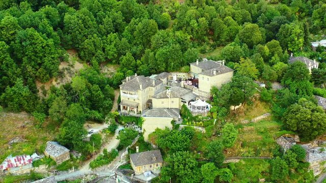 Drone flying backwards over the small village Mikro Papigo in Greece. The village is settled on a hillside, among a forest with a lot og lush green trees