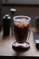 Ice coffee in a tall glass with cream poured over and coffee beans on a old rustic wooden table. Cold summer drink.