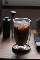 Ice coffee in a tall glass with cream poured over and coffee beans on a old rustic wooden table. Cold summer drink.