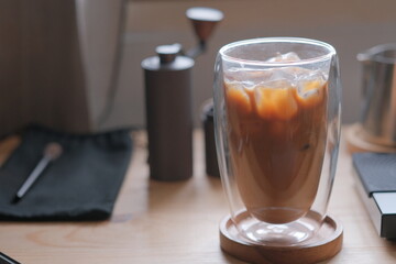 Ice coffee in a tall glass with cream poured over and coffee beans on a old rustic wooden table. Cold summer drink.