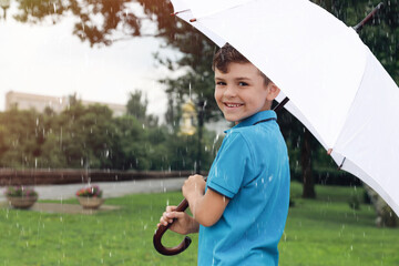 Little boy with umbrella walking under rain in park