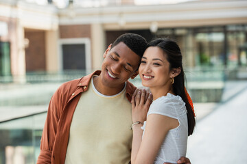 happy african american man with closed eyes near smiling asian woman