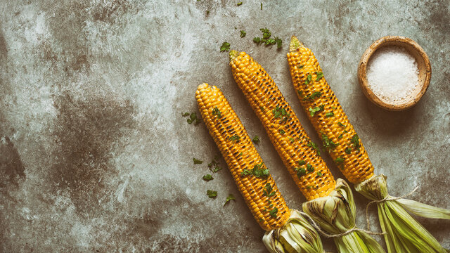 Grilled sweet corn on a dark grunge background. Vegan and vegetarian food. Toned image. Top view, flat lay. Rustic style.