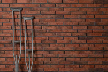Pair of axillary crutches near red brick wall. Space for text