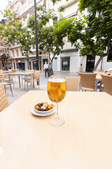 una copa de cerveza fria con una tapa de aceitunas, en una mesa de un restuarante al aire libre