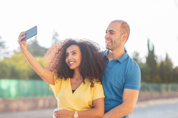 Black woman and white man, cheerful and happy couple taking a selfie shot in a city.