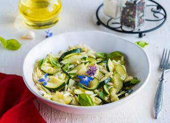 Salad with orzo pasta, fried zucchini and garlic with olive oil dressing in a ceramic bowl on a light concrete background. Orzo salads.