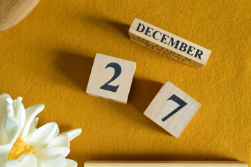 December 27, Wooden Calendar cube on yellow felt fabric with peony flower for date icon background.