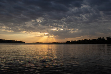 The rays of the setting sun penetrate the clouds on the river