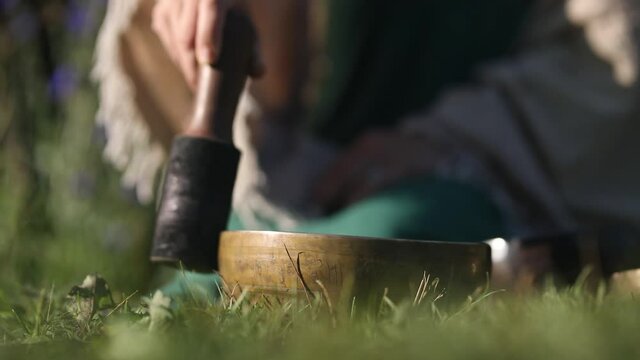 a woman drives a wooden stack over a singing Tibetan bowl in which the mantra "om mani padme hum" is written 