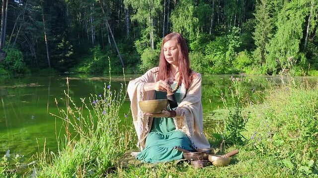 a yogi woman in nature holds a singing massage cup on which the mantra "om mani padme hum" is written 