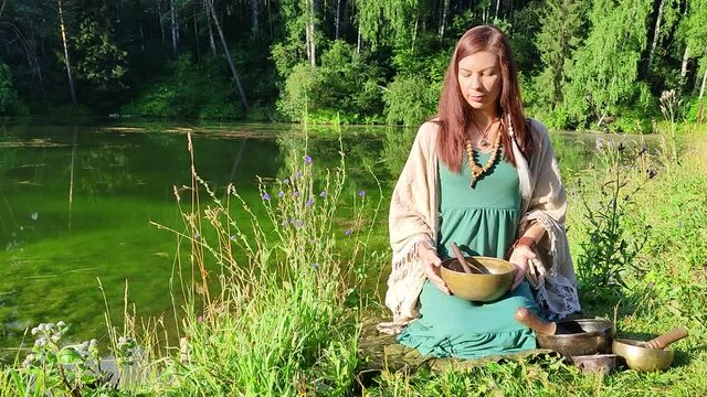a yogi woman in nature holds a singing massage cup on which the mantra "om mani padme hum" is written 
