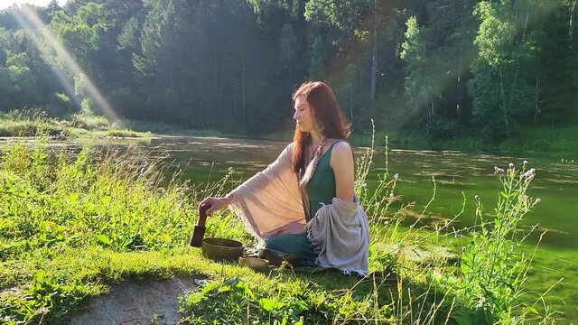 a yogi woman in nature holds a singing massage cup on which the mantra "om mani padme hum" is written 