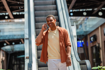 happy african american man talking on smartphone near escalator