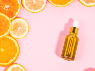 Vitamin C serum bottle with dropper on pink background with orange citrus slices
