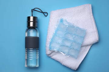 Bottle of water, ice pack and towel on light blue background, flat lay. Heat stroke treatment
