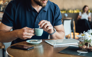 Unrecognizable Businessman Using Digital Tablet while Drinking Coffee in a Cafe.
Close up photo of a anonymous business man drinking espresso and using tablet while sitting and working in a restaurant