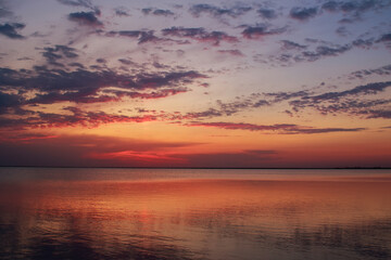 Naklejka premium Dreamy and dramatic colorful sunset sky over calm water surface with cloud reflections