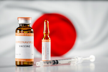 Ampoule of the vaccine against covid-19 coronavirus infection and a syringe on the background of the flag of Japan. Vaccination and immunization in Japan against the virus