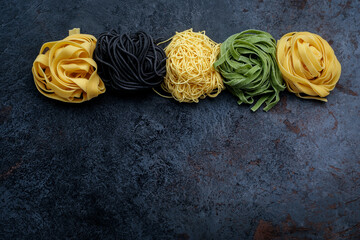 Different types of colorful pasta on a stone background. Uncooked pappardelle, spaghetti, capellini and tagliatelle pasta, top view and copy space