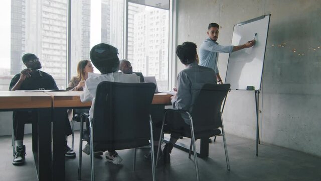 Hispanic man businessman coach gives corporate presentation for diverse multiracial businesspeople in office, ethnic leader boss presents business plan idea on whiteboard speaking to clients investors