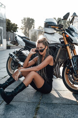 Plakat Woman with motorbike sitting on asphalt on sidewalk