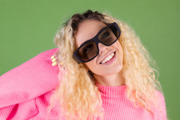 Young blonde woman with long curly hair in pink sweater on green background in 3d  cinema glasses playful smile  happy positive