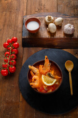 Tom yam soup with shrimps and coconut milk on the table on a round board near milk mushrooms and tomatoes.