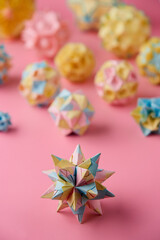 Set of multicolor handmade modular origami balls or Kusudama Isolated on pink background. Visual art, geometry, art of paper folding, paper crafts. Close up, selective focus, copy space.