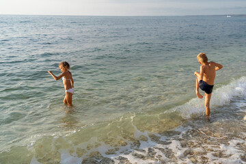 Fototapeta na wymiar Two kids playing on gravel beach at sea in bright sunshine